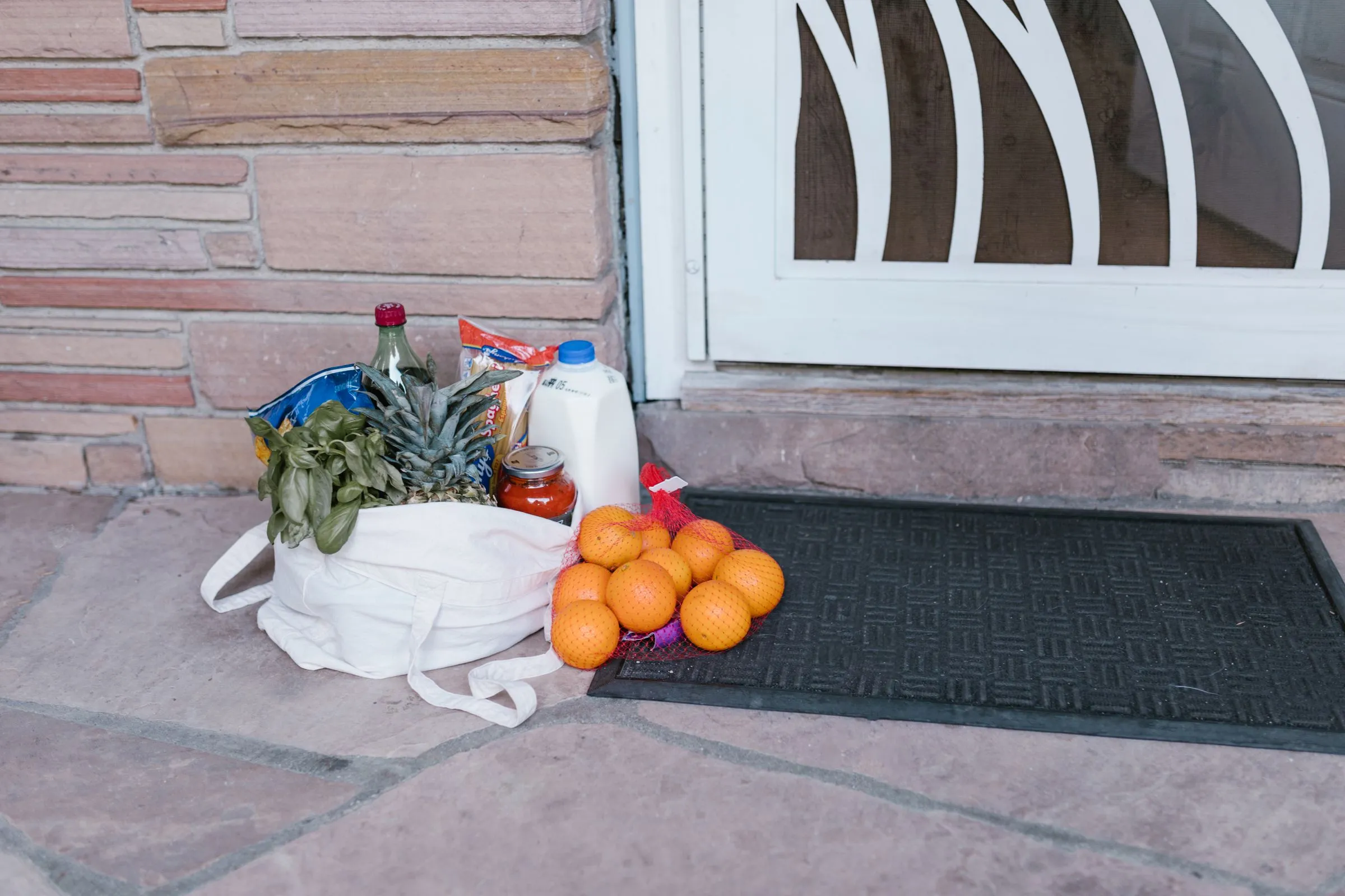 A bag of groceries, oranges and milk left on a doormat